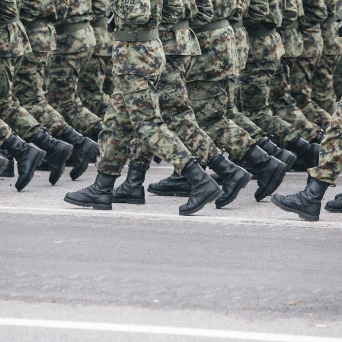 Soldaten maschieren auf Asphalt in eine Richtung. Zu sehen sind ihre Beine im synchronen Schritt