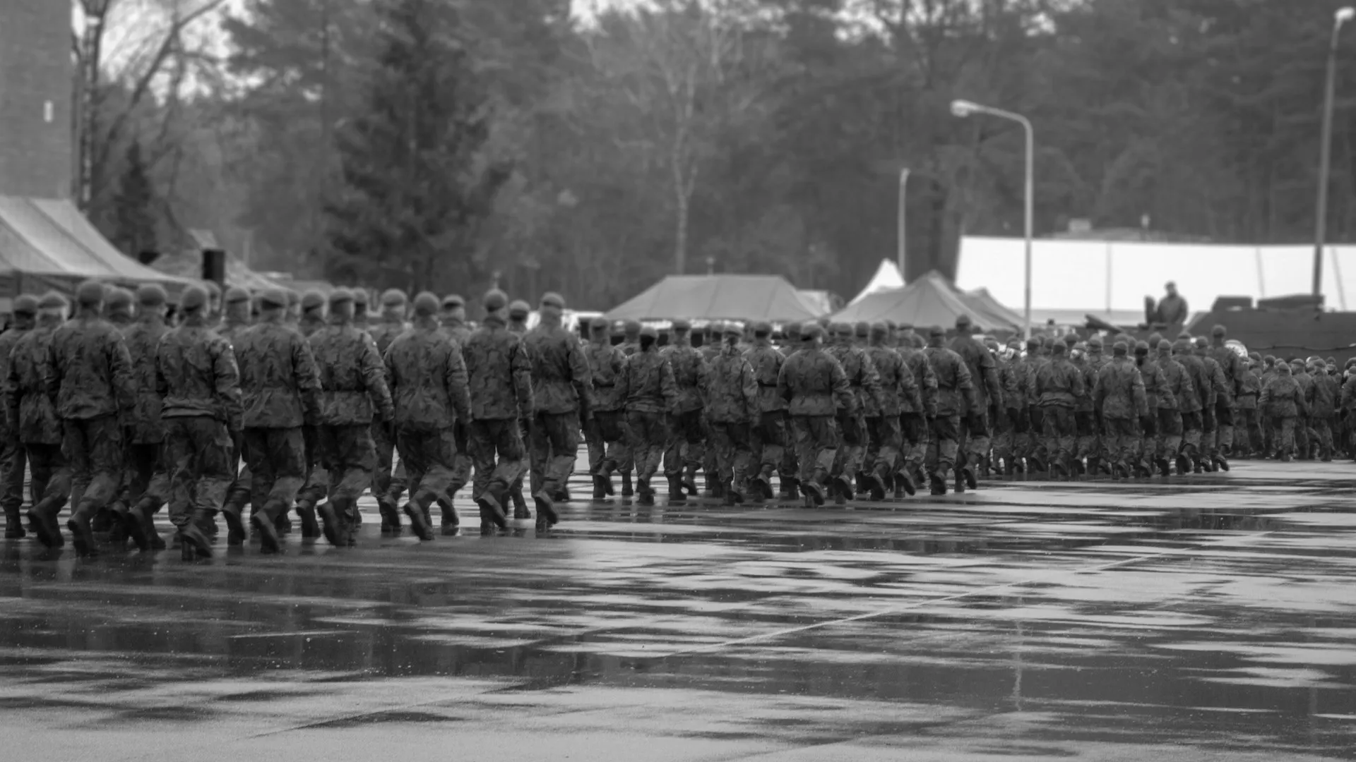 Schwarz Weiss Fotografie. Soldat:innen maschieren im Gleichschritt diagonal weg vom Betrachter. Sie tragen Uniform aber keine Kampfausrüstung